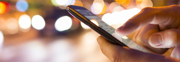 Close-up of a person's hand holding a smartphone while navigating the streets during the late evening.